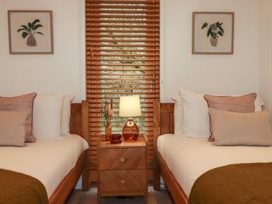 A bedroom with two beds a wooden nightstand and a window with blinds at 1 Streamside in Lanreath