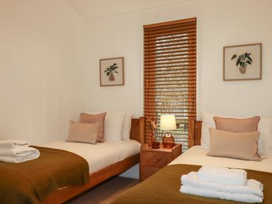 A bedroom with two single beds a wooden nightstand with a lamp and window blinds at 1 Streamside in Lanreath