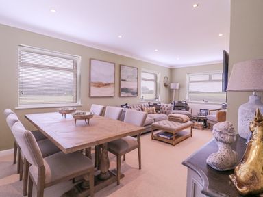 A dining table with chairs and a living room with sofas and a coffee table at The Farmhouse in St Osyth