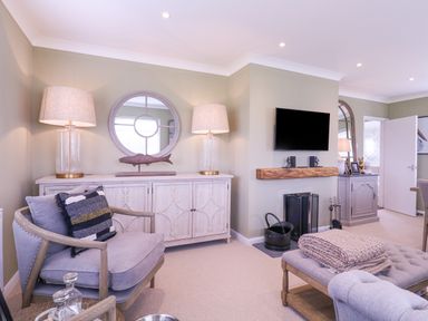 A living room with armchair a wooden cabinet a wall-mounted television and fireplace at The Farmhouse in St Osyth