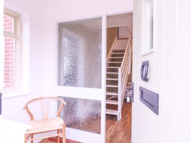 An entryway with a wooden chair a textured glass sliding door and a view of a wooden staircase at The Farmhouse in St Osyth