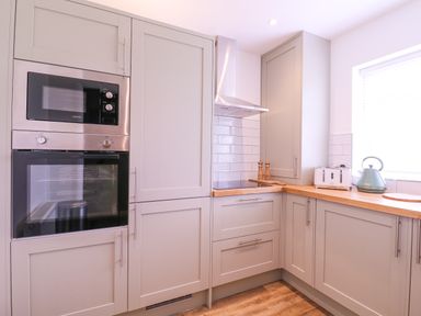 A kitchen with built-in microwave and oven cabinets wooden countertops kettle and toaster next to a window at The Farmhouse in St Osyth