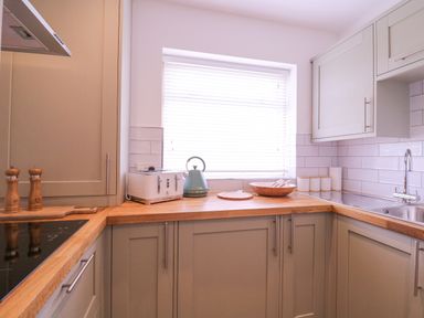 A kitchen with wooden countertops a sink a toaster a kettle and containers at The Farmhouse in St Osyth