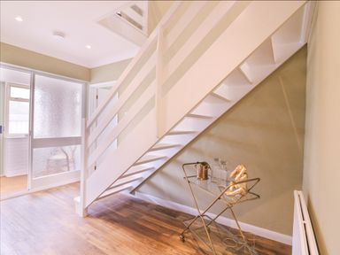 A hallway with white stairs and a glass bar cart under the stairs at The Farmhouse in St Osyth