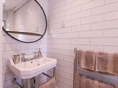 A bathroom sink with a round mirror soap dispenser and metal tumbler and towels on a rack at The Farmhouse in St Osyth