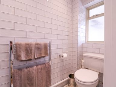 A bathroom with a toilet a window a towel rack with two brown towels and a toilet paper holder at The Farmhouse in St Osyth