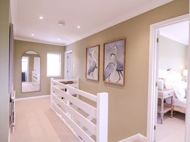 A hallway with a railing mirror and bird paintings next to a bedroom at The Farmhouse in St Osyth
