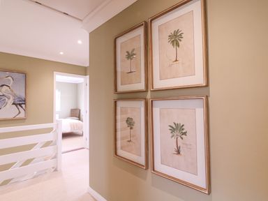 A hallway with four framed palm tree prints on the wall and a view into a bedroom at The Farmhouse in St Osyth