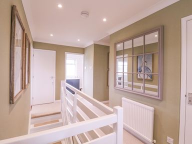 A hallway with a white railing a large mirror on the wall and framed pictures at The Farmhouse in St Osyth