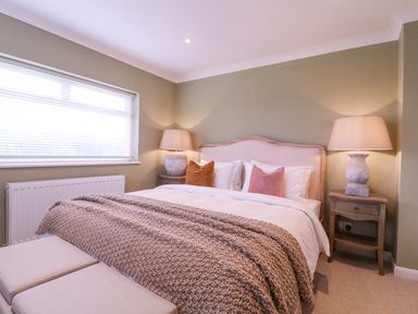 A bedroom with a double bed two bedside tables with lamps a window and a knitted blanket at The Farmhouse in St Osyth