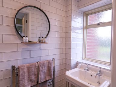 A bathroom with a sink a round mirror on the wall and two towels hanging on a rack at The Farmhouse in St Osyth