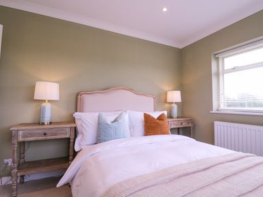 A bedroom with a bed, pillows, bedside tables with lamps, and a window at The Farmhouse in St Osyth
