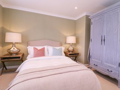 A bedroom with a double bed flanked by two wooden bedside tables with lamps and a grey wooden wardrobe at The Farmhouse in St Osyth