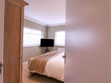 A bedroom with a bed covered with a knit blanket a wooden wardrobe and a television on a stand at The Farmhouse in St Osyth