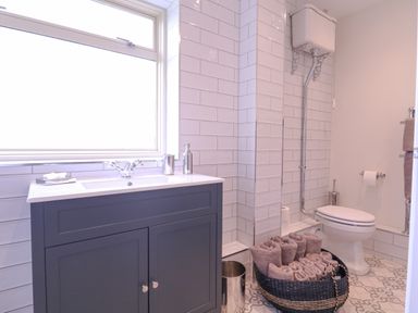 A bathroom with a sink cabinet and a toilet next to a basket of towels at The Farmhouse in St Osyth