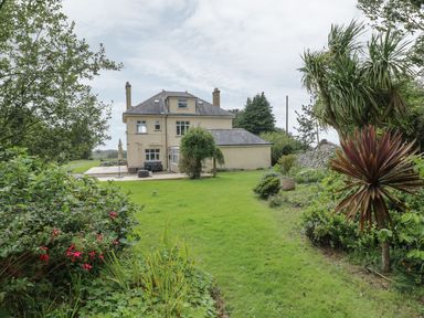 A garden with grass and various plants behind a two-story house at Tan Y Fron in Dyffryn Ardudwy