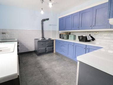 A kitchen with blue cabinets white countertops a gray stove and tiled backsplash at Tan Y Fron Dyffryn Ardudwy