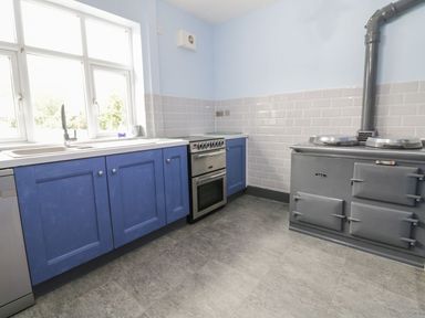 A kitchen with blue cabinets a sink a stove and a gray Aga cooker at Tan Y Fron in Dyffryn Ardudwy