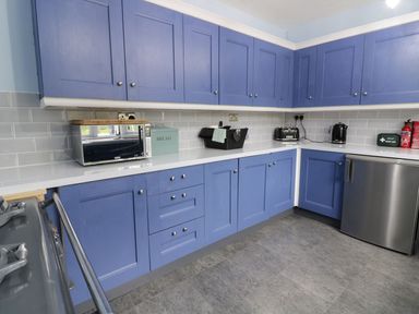 A kitchen with blue cabinets a microwave toaster kettle first aid kit and fire extinguisher at Tan Y Fron in Dyffryn Ardudwy