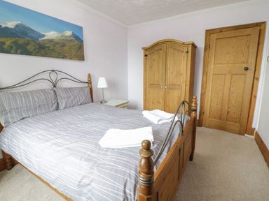 A bedroom with a double bed gray striped bedding wooden wardrobe wooden door and a table lamp at Tan Y Fron in Dyffryn Ardudwy