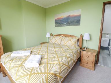 A bedroom with a double bed with patterned bedding two bedside tables with lamps and a door to a bathroom at Tan Y Fron in Dyffryn Ardudwy