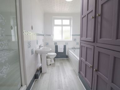 A bathroom with a sink toilet bathtub a window and purple cabinets at Tan Y Fron in Dyffryn Ardudwy
