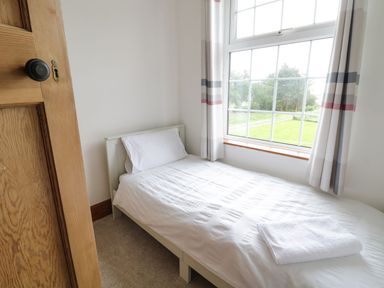 A single bed with white linens and a folded towel next to a window with curtains in a small bedroom at Tan Y Fron in Dyffryn Ardudwy