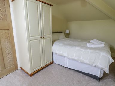 A bedroom with a double bed with white bedding and two folded towels a cream wardrobe a wooden door and a floor lamp at Tan Y Fron in Dyffryn Ardudwy