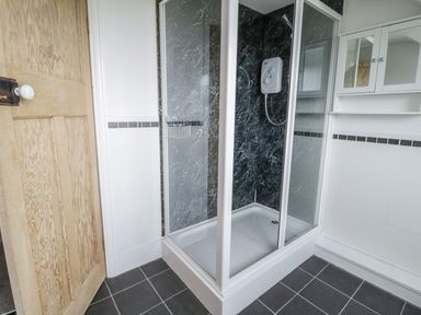 A bathroom shower cubicle with black marble walls and a white cabinet with mirrored doors at Tan Y Fron in Dyffryn Ardudwy