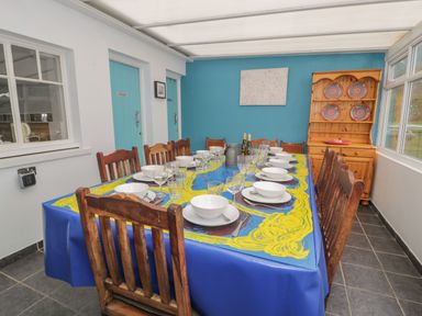 A dining room with a long table set with plates bowls and glasses surrounded by wooden chairs and a wooden cabinet with decorative plates at Tan Y Fron in Dyffryn Ardudwy