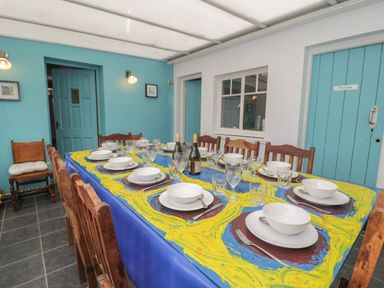 A dining area with a long table set for twelve people with blue and yellow tablecloth at Tan Y Fron in Dyffryn Ardudwy