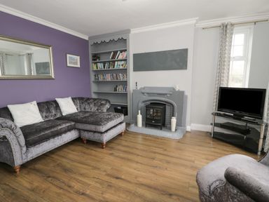 A living room with a grey sectional sofa a bookshelf a fireplace and a TV on a stand at Tan Y Fron in Dyffryn Ardudwy