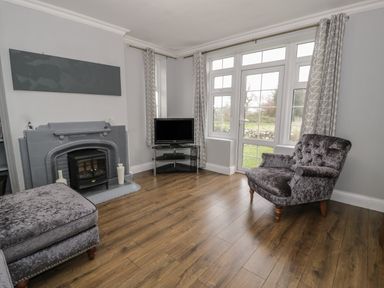 A living room with a fireplace television armchair and window with curtains at Tan Y Fron in Dyffryn Ardudwy