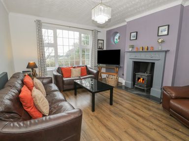 A living room with brown leather sofas orange and beige cushions a black coffee table a fireplace with a wood burning stove and a flat screen TV at Tan Y Fron in Dyffryn Ardudwy