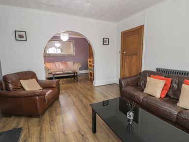 A living room with brown leather sofas a black coffee table wooden floor and an archway leading to another seating area at Tan Y Fron in Dyffryn Ardudwy