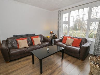 A living room with two brown leather sofas with orange and beige cushions a black glass coffee table a lamp on a side table and large windows at Tan Y Fron in Dyffryn Ardudwy