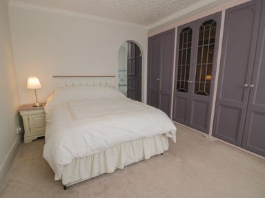 A bedroom with a bed and nightstand with lamp next to built in wardrobes at Tan Y Fron in Dyffryn Ardudwy