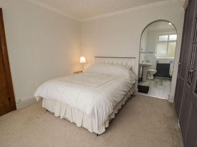 A bedroom with a bed a bedside lamp an arched doorway leading to a bathroom and a purple wardrobe at Tan Y Fron in Dyffryn Ardudwy