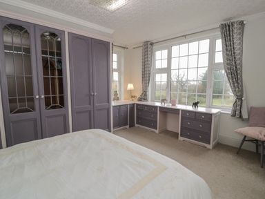 A bedroom with built-in gray wardrobes a window desk with drawers a bed and a chair near the window at Tan Y Fron in Dyffryn Ardudwy
