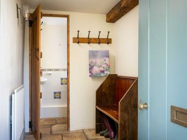 A hallway with an open door revealing a bathroom with tiled walls a wooden bench with boots underneath and a wall-mounted coat rack at Hope Cottage in Longborough