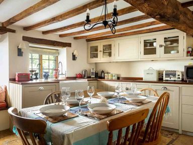 A kitchen with a dining table set with plates glasses and cutlery under exposed wooden ceiling beams at Hope Cottage in Longborough