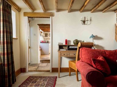 A living room with a red sofa a wooden desk and chair and a view into a kitchen at Hope Cottage in Longborough