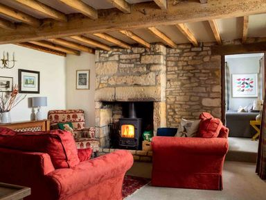 A living room with red sofas a stone fireplace and wood burning stove at Hope Cottage in Longborough