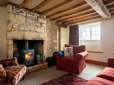 A living room with a stone fireplace a wood-burning stove and upholstered chairs at Hope Cottage in Longborough