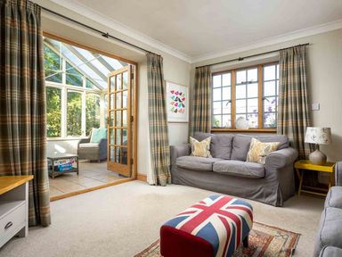 A living room with a gray sofa pillows a lamp and an ottoman with a Union Jack pattern at Hope Cottage in Longborough