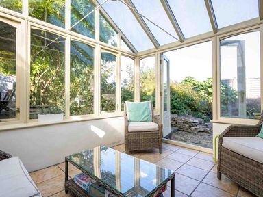 A conservatory with wicker chairs and a glass coffee table opening to a garden at Hope Cottage in Longborough