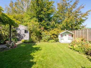 A garden with a green lawn two sheds wooden fence and trees at Hope Cottage in Longborough