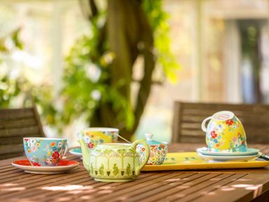 A wooden outdoor table set with floral teacups saucers a teapot and a sugar bowl at Hope Cottage in Longborough