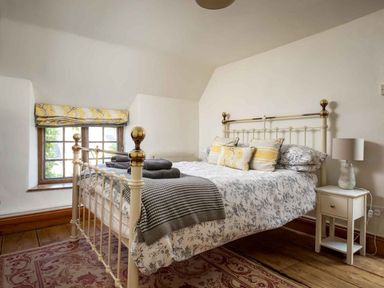 A bedroom with a metal bed a side table with a lamp and a window with a yellow patterned blind at Hope Cottage in Longborough