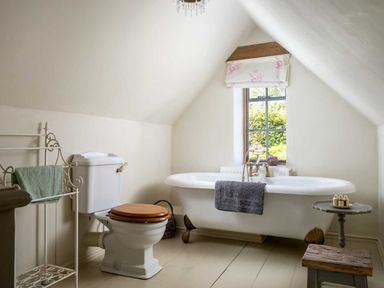 A bathroom with a toilet a freestanding bathtub and a small table by a window at Hope Cottage in Longborough